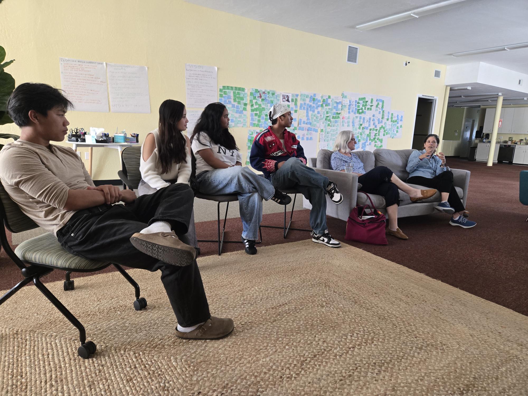 students sit in a circle of chairs at the Center and discuss a project
